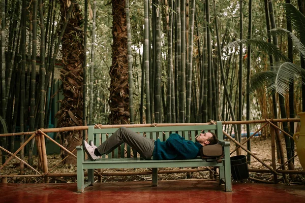 Backpacker man lying on a bench. Man lying on a bench in nature with backpack. Tourist lying on a bench