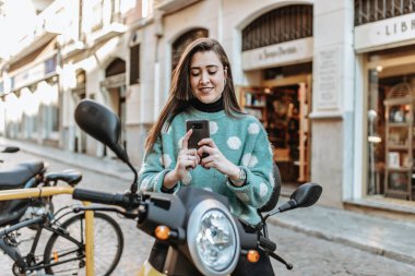 Cep telefonu kullanarak motosiklet üzerinde güzel bir kadın. Tipik bir haber motosiklet üzerinde oturan bir bayan. Kadın iş gününün bitiş
