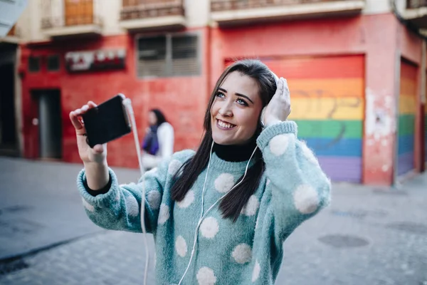 Piękna Kobieta Słuchanie Muzyki Przez Słuchawki Biorąc Selfie Ulicy — Zdjęcie stockowe