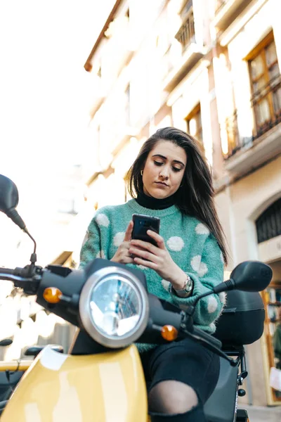 Cep telefonu kullanarak motosiklet üzerinde güzel bir kadın. Tipik bir haber motosiklet üzerinde oturan bir bayan. Kadın iş gününün bitiş