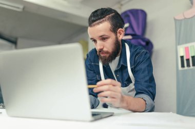Genç hipster usta el sanatları Atölyesi içinde belgili tanımlık bilgisayar perde gösteriyordu. Tasarımcı atölyesinde çalışan dizüstü bilgisayar ekranında arıyorum.