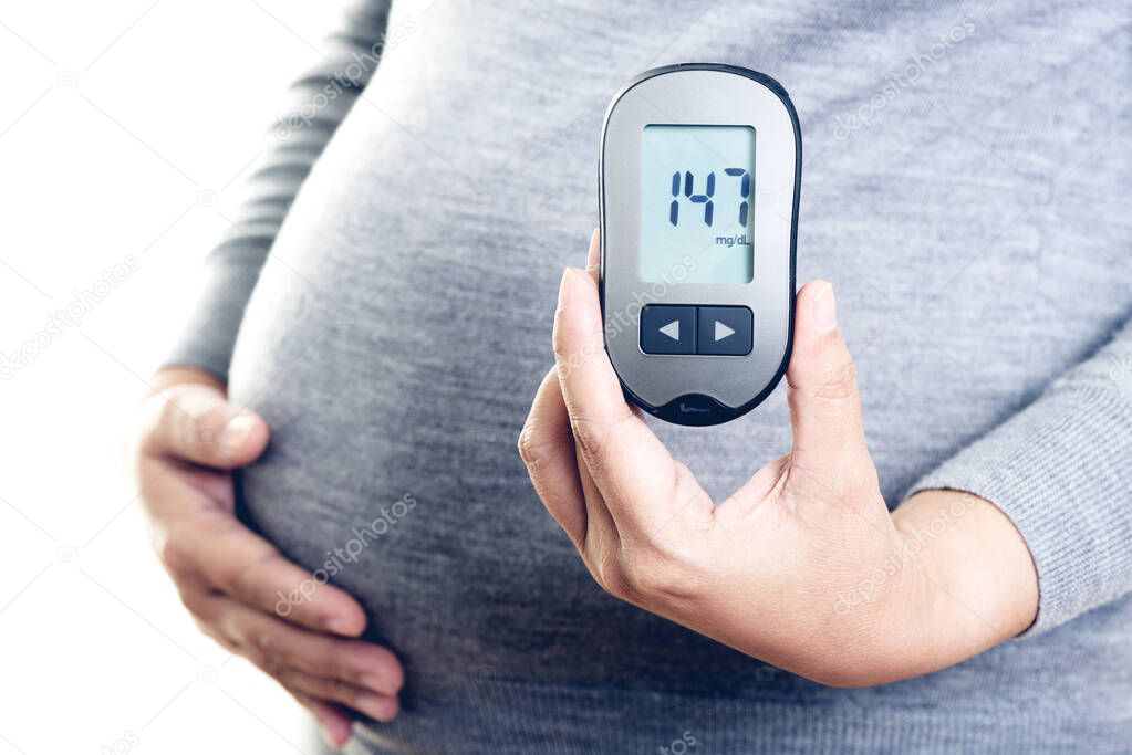Pregnant woman checking blood sugar level with blood glucose meter. Gestational diabetes.