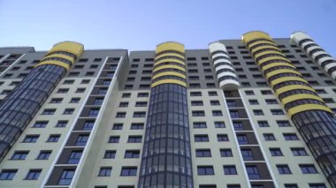 Kiralık ev. Açık mavi gökyüzüne karşı modern bir apartman binasının ön cephesi. Düşük açılı çekim. Alışılmadık bir tasarımı olan, sarı eklemli bir bina..