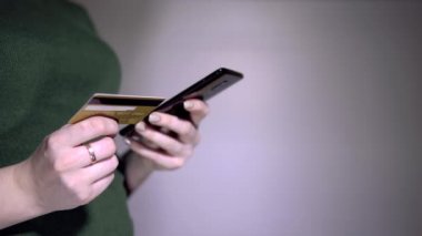 Yeşil tişörtlü bir kadın internet üzerinden akıllı telefon ve kredi kartı kullanarak online ödeme yapıyor. Kız banka kartı numarasından akıllı telefona giriş yapıyor. 4km 'lik atış. Kapat..