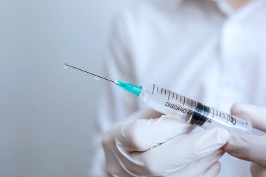 Beyaz eldivenli doktor elinde şırınga tutuyor.