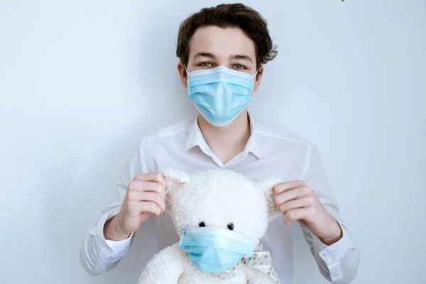 a guy in a medical mask with medical gloves holds a soft toy in a mask, a bear in a mask