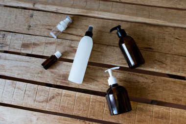 Kozmetik ürünleri için konteynırlar ahşap bir masanın üzerinde uzanıyor. Kravat kağıdı, sprey, yağ, jel, kahverengi cam, kozmetik bileşimi.