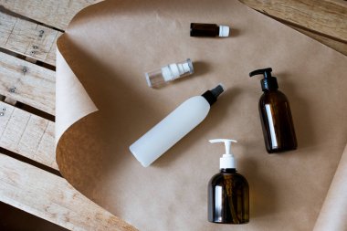 Kozmetik ürünleri için konteynırlar ahşap bir masanın üzerinde uzanıyor. Kravat kağıdı, sprey, yağ, jel, kahverengi cam, kozmetik bileşimi.