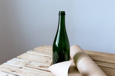 Ahşap bir masanın üzerinde yeşil bir şişe ve beyaz bir arka planda bir rulo el işi kağıt.