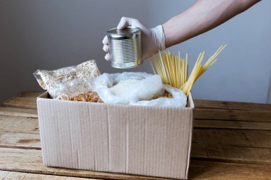 Karton kutuda ürünler, karantinaya alınmış yiyecekler, izolasyon için gerekli ürünler, karbonhidratlar, market seti, bir insan ürünleri bir kutuya koyar.