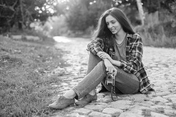 Black and white photo young woman sitting on paving stone road with camera