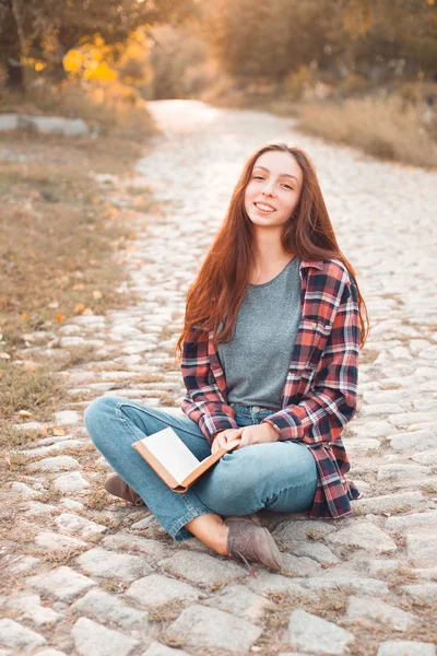 young woman sitting on paving stone road with book