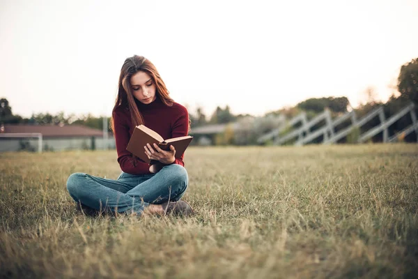 stadyum alanında oturup ve kitap okuma genç kadın