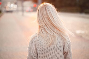 Arkadan görünüşü günbatımı sırasında caddenin üzerinde yürüyen genç sarışın kadın