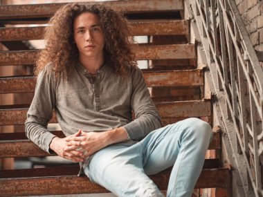 kıvırcık saçlı paslı merdivenlerde oturan genç adam