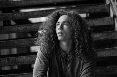 Tek renkli kıvırcık saçlı paslı merdivenlerde oturan genç adam portresi