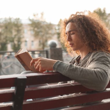 Genç adam parkta kitap okuyor.