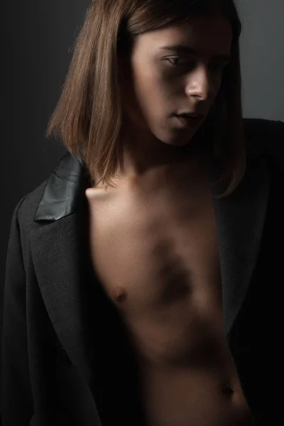 portrait of androgynous young man in coat on dark background