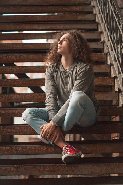 young man with curly hair sitting on rusty stairs