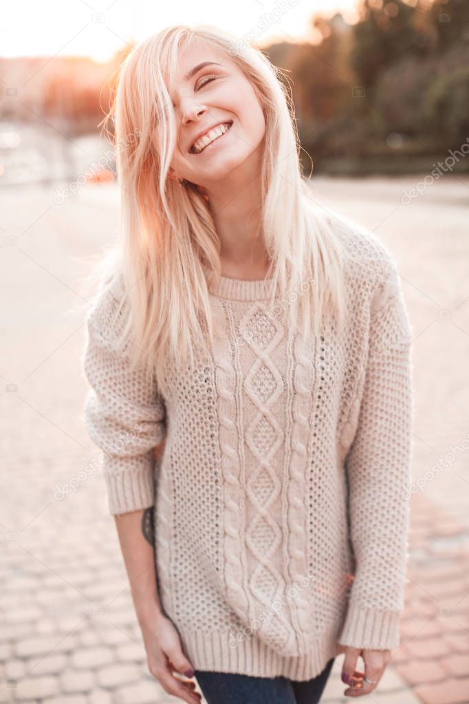Smiling young blond woman walking on city street during sunset