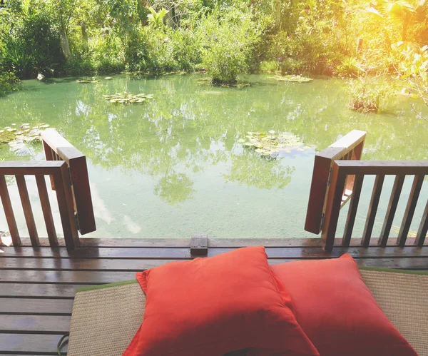 Drewniane patio na relaksujący zielony staw z mata podłogowa bambus i jasne pomarańczowe poduszki — Zdjęcie stockowe