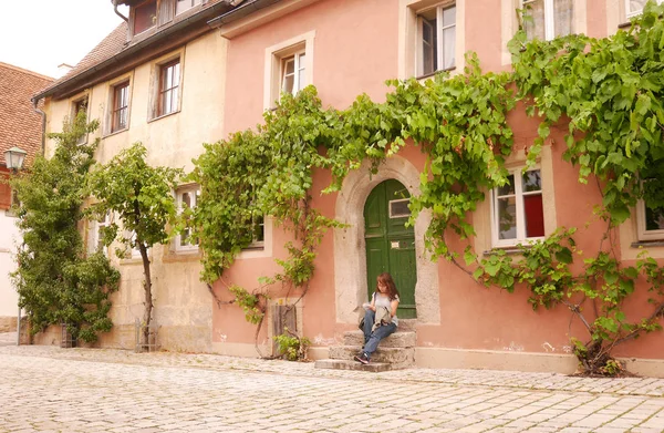 Bavyera, Almanya - 21 Temmuz 2016: Asyalı kadın yalnız seyahat seyahat güzergah belgeleri bir ev Rothenburg Ob Der Tauber, ünlü turizm şehir Franconia bölgesinde sokakta bir kapı adımlar üzerinde otururken arıyorsunuz