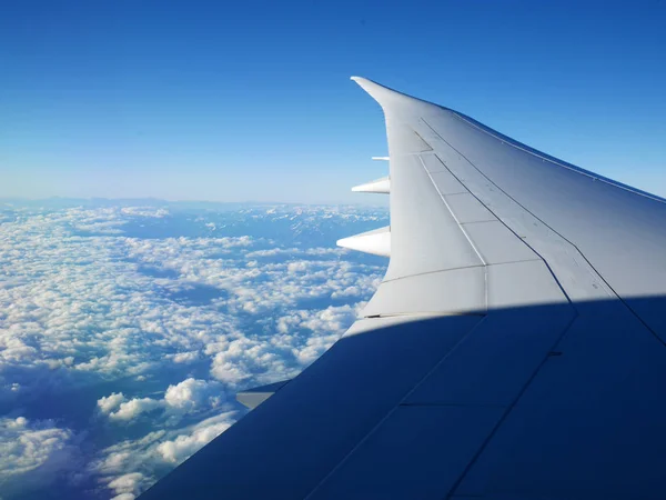 Ala de avión y cielo azul con hermosas nubes debajo y montañas en el fondo — Foto de Stock
