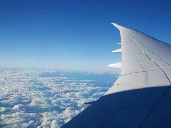 Asa de avião e céu azul com belas nuvens embaixo e montanhas no fundo — Fotografia de Stock