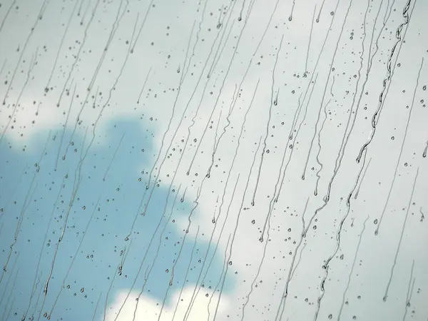 Gocce di pioggia in esecuzione su vetro con cielo blu e sfondo nuvola bianca — Foto Stock