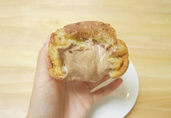 Ev yapımı Japon choux krem puf, lezzetli çikolata içinde doldurma bol görmek yarısı. Fırına bir kadın eli üzerinde arka planda ahşap masa üzerinde beyaz plaka ile düzenlenmektedir