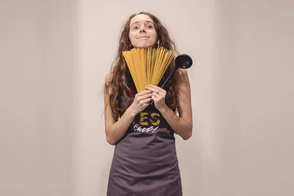 Komik kız gri önlük spagetti ve gülümseyen fan dışında görünüyor. Diğer elinde kaşık elinde
