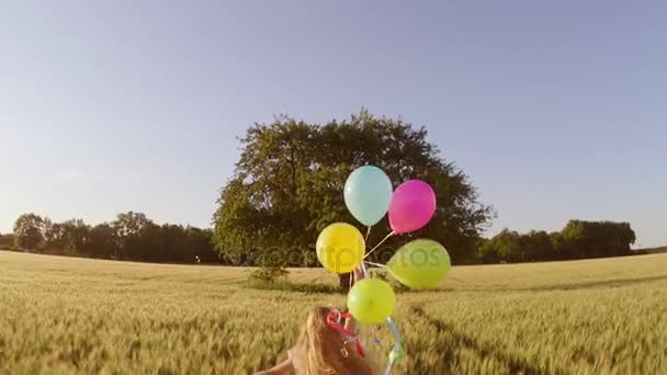 大きな木に麦畑の中 色とりどりの風船の束を保持の十代の少女のリアビュー映像 — ストック動画