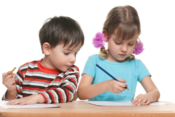 Niños en edad preescolar se sientan en el escritorio y escriben —  Fotos de Stock