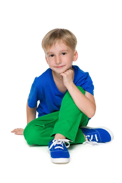 Blond liten pojke i gröna byxor sitter — Stockfoto