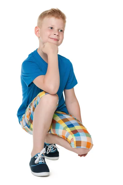Handsome little boy in a blue shirt sits — Stock Photo, Image