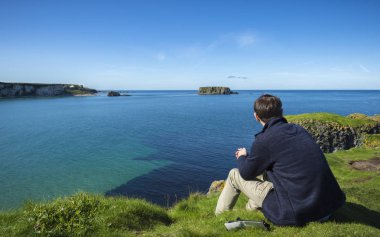 Kırmızı bir Carrick denizde seyir bir uçurumun kenarında oturan bir adam