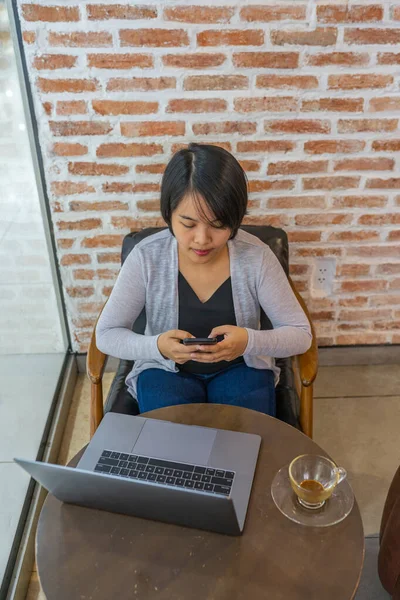 Mujer asiática mirando la pantalla del teléfono inteligente mientras está sentado con el ordenador portátil — Foto de Stock