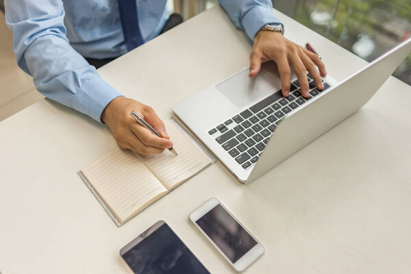 Бизнесмен работает над ноутбуком и пишет заметки
