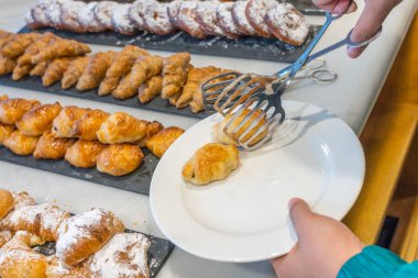 Mini kruvasan toplayan maşa kullanan bir kadın.