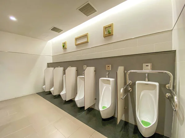 Современный мужской туалет с белым фарфоровым писсуаром в очереди — стоковое фото