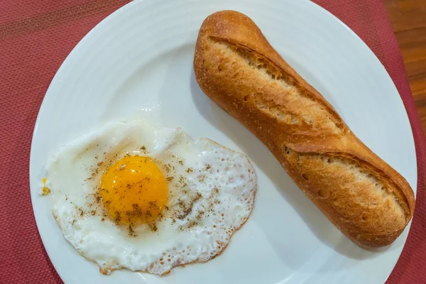 Багетный хлеб и солнечное яйцо на белой тарелке на завтрак — стоковое фото