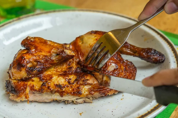 People using knife cutting grilled chicken leg on white plate — Stock Photo, Image