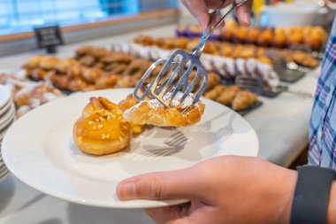 Kahvaltı büfesinde insan kruvasan topluyor. 