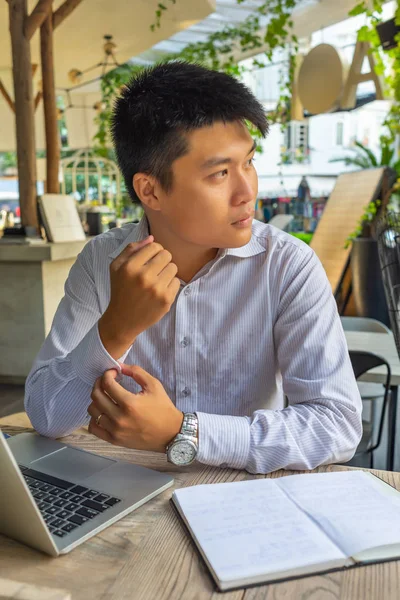 年轻的亚洲商人坐在咖啡店里，手里拿着笔记本电脑和笔记本 — 图库照片