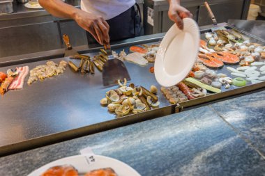 Barbekü büfesi şefi büyük tavada çeşitli deniz ürünleri pişiriyor.