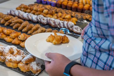 Kahvaltı büfesinde hamur işi kruvasanı seçen insanlar.
