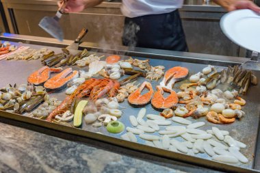 The chef grilling various kinds of seafood on big pan