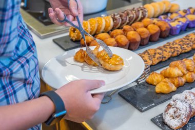 Açık büfe partisinde tabağına karamelli çörek koyan bir insan.