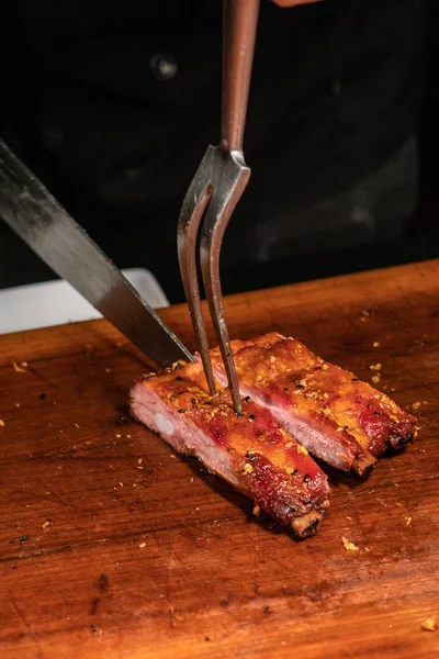 Вертикальное фото шеф-повара барбекю, режущего острые ребра на гриле — стоковое фото