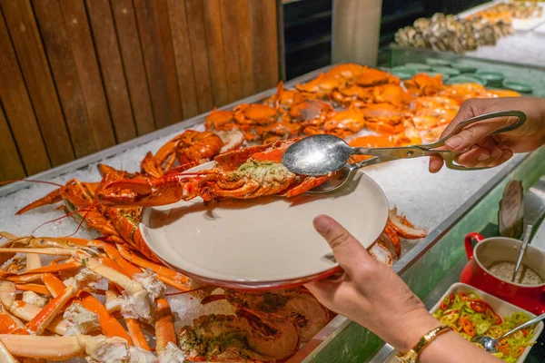 Mano donna con pinze per raccogliere l'aragosta a buffet di frutti di mare — Foto Stock